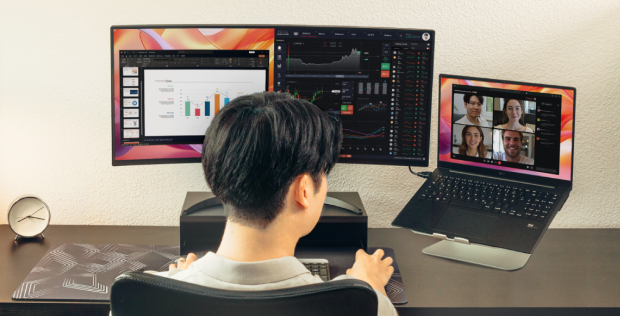 Person working remotely at a dual monitor setup desk, with LG monitor and a laptop showing a video meeting