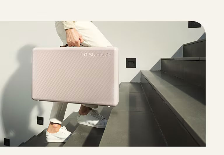 A man is carrying the LG StanbyME Go thanks to its carry bag design.