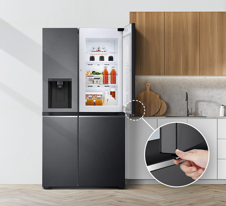 A front view of the refrigerator installed in a kitchen. The top right door is open and there is a circle and a line leading to a larger circle that shows a magnified view of the button on the bottom left corner of the open door which has a concealed opening button.
