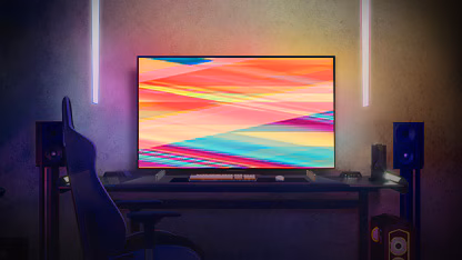 صورة يظهر بها تلفزيون OLED C2 من إل جي في غرفة مضاءة بدفء في الليل مع أرائك، والكثير من الوسائد، ومصباح، وطاولة جانبية ومجموعة من النباتات.