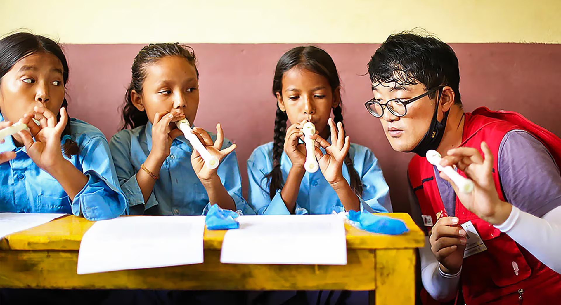 LG volunteers in a red vest tell us how to play the recorder to three children.