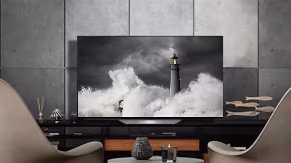 LG OLED B2 is in a gray room with stone walls, accessories, and chairs facing on to it
